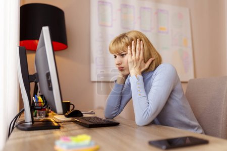 Woman working in an office sitting at her desk stressed out and exhausted while working overtime to meet a project deadline