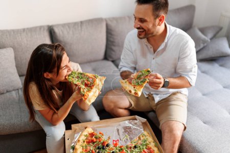 Photo for Beautiful young couple in love relaxing at home, eating pizza and having fun spending time together - Royalty Free Image