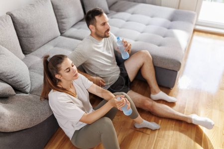 Téléchargez les photos : Couple prendre une pause tout en faisant de l'exercice ensemble à la maison, boire de l'eau et se préparer pour l'entraînement - en image libre de droit