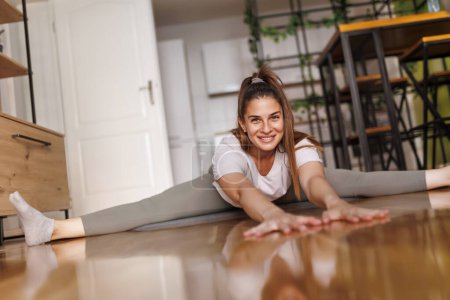 Photo for Low angle view of young woman in sportswear stretching out on yoga mat after doing home workout - Royalty Free Image