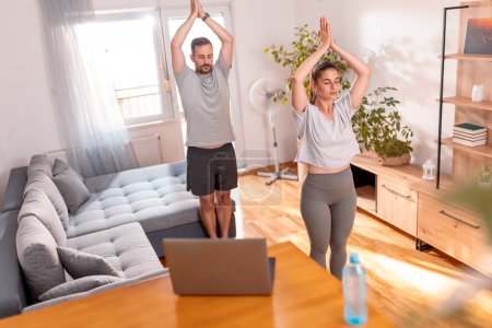 Foto de Pareja joven haciendo ejercicio juntos en casa, haciendo clases de yoga en línea como rutina de ejercicios matutinos - Imagen libre de derechos