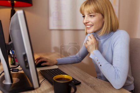 Téléchargez les photos : Femme assise à son bureau à la maison travaillant à l'aide d'un ordinateur de bureau, ayant une réunion par conférence téléphonique - en image libre de droit