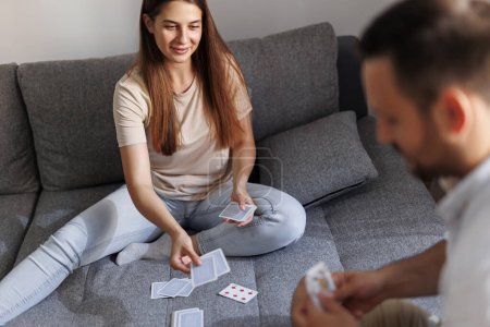 Foto de Hermosa pareja joven enamorada disfrutando de su tiempo libre en casa juntos y divirtiéndose jugando juegos de cartas - Imagen libre de derechos
