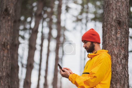 Téléchargez les photos : Homme actif surfant sur Internet à l'aide d'un téléphone intelligent tout en se relaxant à l'extérieur après une course matinale dans le parc par une journée d'automne nuageuse - en image libre de droit