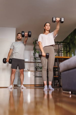 Photo for Active couple working out at home doing arms exercises lifting weights - Royalty Free Image