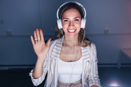 Photo for Business woman sitting at her desk wearing headset having online meeting while working late in an office - Royalty Free Image