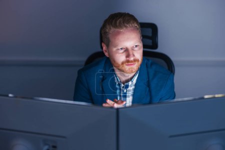 Photo for Confident successful businessman sitting at his desk using desktop computer while working late in an office - Royalty Free Image