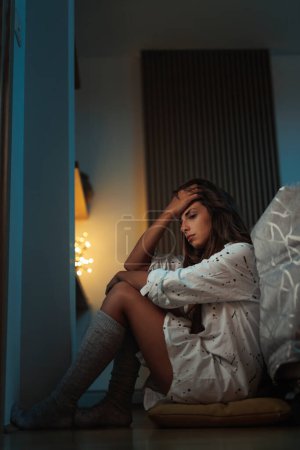 Téléchargez les photos : Femme déprimée assise par terre près du lit, la tête dans les mains stressée et anxieuse - en image libre de droit