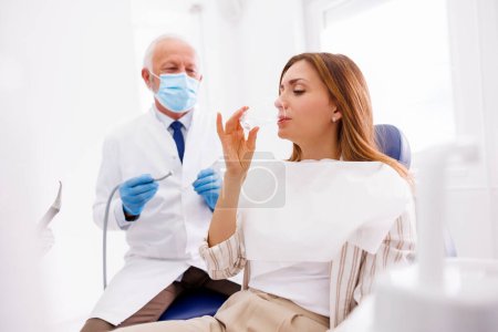 Téléchargez les photos : Dentiste fixer la dent du patient à la clinique dentaire à l'aide d'une perceuse dentaire et miroir incliné, patient assis à la chaise dentaire et laver la cavité buccale - en image libre de droit