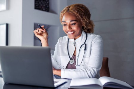 Téléchargez les photos : Médecin féminin ayant une consultation par appel vidéo en ligne avec le patient tout en travaillant à distance à partir du bureau à domicile, le télétravail - en image libre de droit