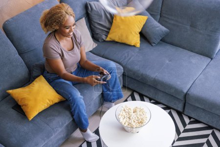 Photo for High angle view of cheerful woman sitting on living room sofa having fun spending leisure time at home playing video games - Royalty Free Image