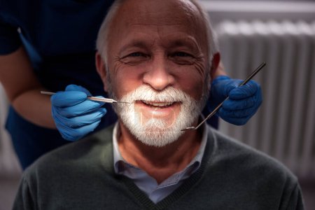 Photo for Doctor checking up patient's teeth at dentist office; senior man at dental checkup - Royalty Free Image