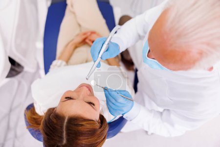 Téléchargez les photos : Vue grand angle du médecin fixant la dent du patient au cabinet du dentiste à l'aide d'une perceuse dentaire et d'un miroir incliné - en image libre de droit