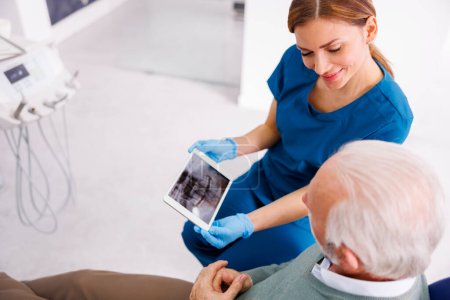 Photo for Doctor showing jaw x-ray on tablet computer to patient sitting in dental chair at dentist office - Royalty Free Image