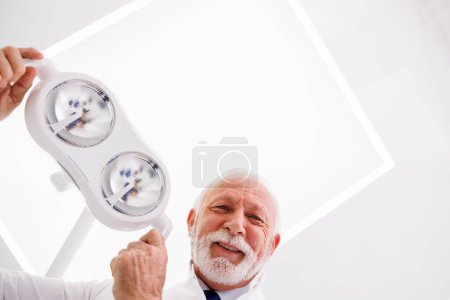 Photo for Low angle view of dentist adjusting reflector lights above patient's head sitting in dental chair - Royalty Free Image