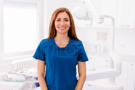 Foto de Retrato de dentista femenina con uniforme de pie clínica dental y sonriente - Imagen libre de derechos