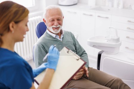 Téléchargez les photos : Homme âgé ayant un examen dentaire au cabinet du dentiste, consulter un médecin au sujet des procédures nécessaires, dentiste prenant des dossiers médicaux - en image libre de droit