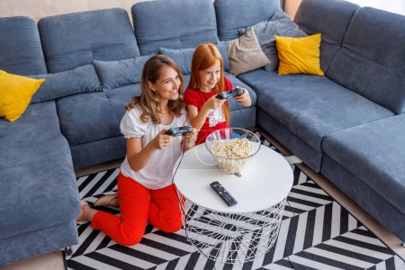 Photo for High angle view of beautiful mother and cute little daughter having fun playing video games while spending leisure time together at home - Royalty Free Image