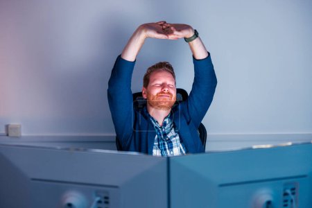 Photo for Tired businessman stretching at his desk while working late at the office - Royalty Free Image