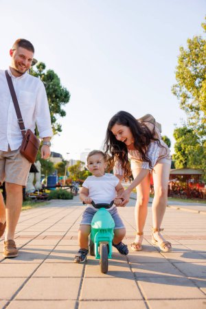 Photo for Beautiful young mother and father having fun spending leisure time outdoors with their child, teaching him to ride a bike - Royalty Free Image
