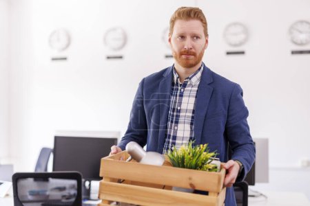 Téléchargez les photos : Homme licencié du travail portant des choses dans la boîte tout en quittant le bureau stressé et triste - concept de chômage et de perte d'emploi - en image libre de droit