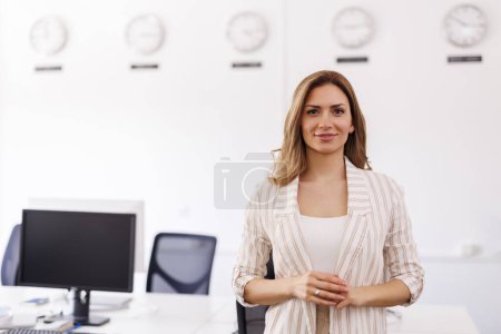 Téléchargez les photos : Entrepreneuse réussie debout dans un bureau et souriant avec les bras croisés ; portrait de femme d'affaires moderne - en image libre de droit