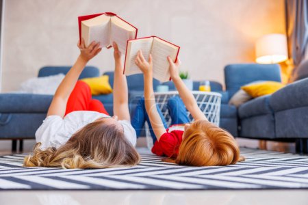 Photo for Beautiful mother and daughter lying on the floor relaxing at home reading books together - Royalty Free Image