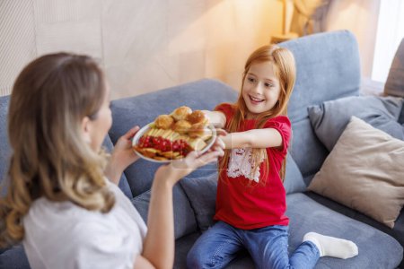 Photo for Mother and daughter enjoying leisure time together at home, eating snacks and having fun - Royalty Free Image