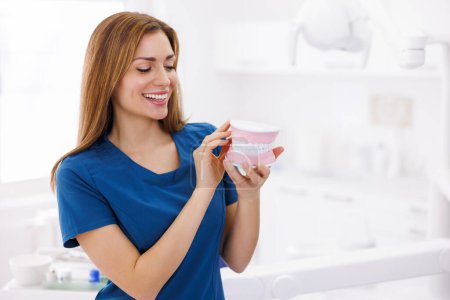 Photo for Portrait of young female dentist wearing uniform standing in dental clinic, holding plastic jaw model and smiling with copy space - Royalty Free Image