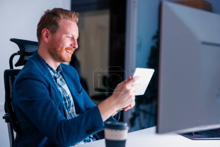 Photo for Casual businessman using tablet computer while working overtime in an office late at night - Royalty Free Image