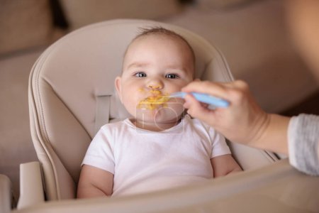 Téléchargez les photos : Mignon bébé garçon assis dans chaise haute tous désordonné et staied refuser de manger porridge - en image libre de droit
