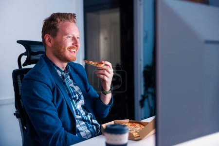 Photo for Successful young businessman eating take away pizza and drinking coffee while working overtime in an office late at night - Royalty Free Image