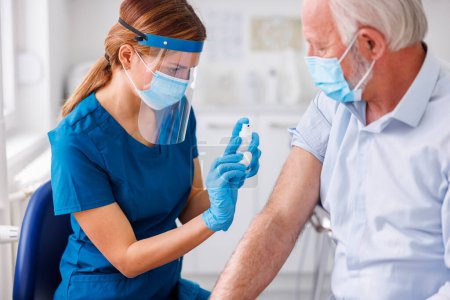 Spécialiste des soins de santé désinfectant le point d'application du vaccin et préparant le patient âgé de sexe masculin à la vaccination