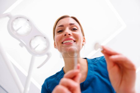 Foto de Vista de ángulo bajo del dentista femenino que sostiene el espejo angulado mientras revisa el diente de los pacientes - Imagen libre de derechos