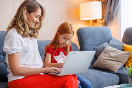 Photo for Mother tutoring daughter at home and helping her with homework using laptop computer for online lessons; homeschooling and distance learning concept - Royalty Free Image