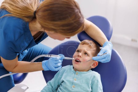 Téléchargez les photos : Une dentiste fixe la dent d'un enfant à l'aide d'une perceuse dentaire et d'un miroir incliné à la clinique dentaire - en image libre de droit