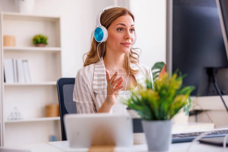 Foto de Mujer de negocios sentada en su escritorio con auriculares que tienen reunión en línea mientras trabaja en una oficina - Imagen libre de derechos