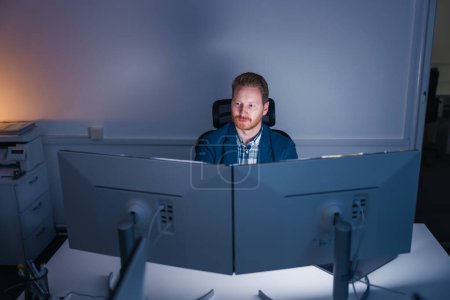 Photo for Confident successful businessman sitting at his desk using desktop computer while working late in an office - Royalty Free Image