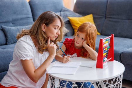 Mother helping daughter with school project and homework, studying math, practicing summation and subtraction together at home
