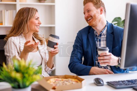 Foto de Compañeros de negocios divirtiéndose tomando un descanso para almorzar en la oficina, comiendo pizza y tomando café - Imagen libre de derechos