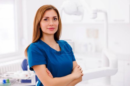 Photo for Portrait of young successful confident female doctor wearing uniform standing in ER and smiling with arms crossed - Royalty Free Image