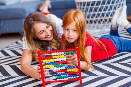 Mother helping daughter with school project and homework, studying math, practicing summation and subtraction using abacus together at home