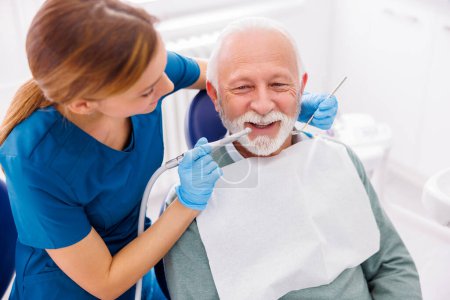 Téléchargez les photos : Dentiste féminine fixant la dent du patient à la clinique dentaire à l'aide d'une perceuse dentaire et d'un miroir incliné - en image libre de droit