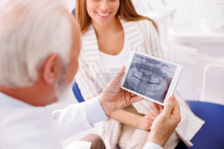 Foto de Médico mostrando rayos X de mandíbula en tableta al paciente sentado en silla dental en el consultorio del dentista - Imagen libre de derechos