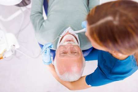 Foto de Vista de ángulo alto del médico que fija el diente del paciente en el consultorio del dentista usando taladro dental y espejo en ángulo - Imagen libre de derechos