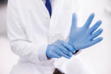 Photo for Doctor putting on protective surgical gloves while working in hospital; dentist putting on medical latex gloves before oral surgery procedure - Royalty Free Image