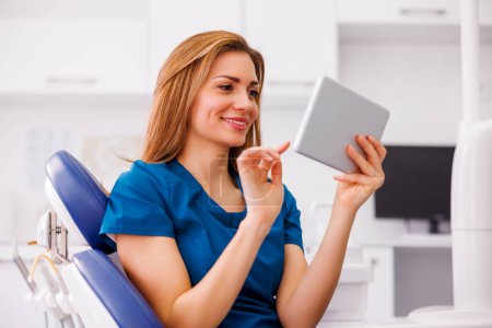 Ärztin in Uniform sitzt mit Tablet-Computer in ER und überprüft Patientenakten und lächelt mit Kopierplatz