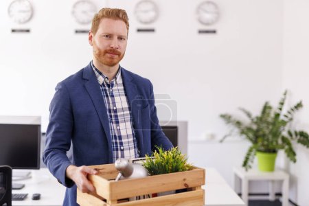 Foto de El hombre despedido del trabajo llevando cosas en caja mientras salía de la oficina estresado y triste - concepto de desempleo y pérdida de empleo - Imagen libre de derechos