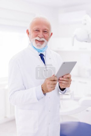 Foto de Retrato de un médico de cabecera con uniforme de pie en el hospital, comprobando las historias clínicas con Tablet PC - Imagen libre de derechos