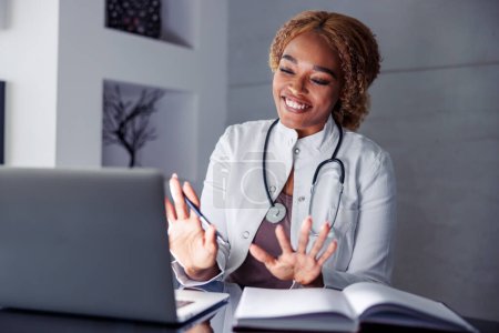 Téléchargez les photos : Médecin féminin ayant une consultation par appel vidéo en ligne avec le patient tout en travaillant à distance à partir du bureau à domicile, le télétravail - en image libre de droit